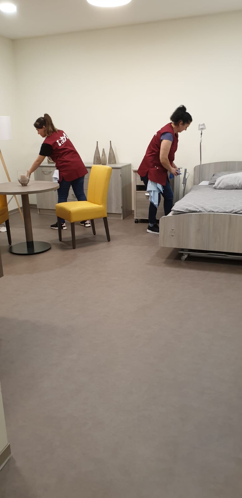 Zwei Mitarbeiterinnen reinigen ein Zimmer mit Bett und Kommode