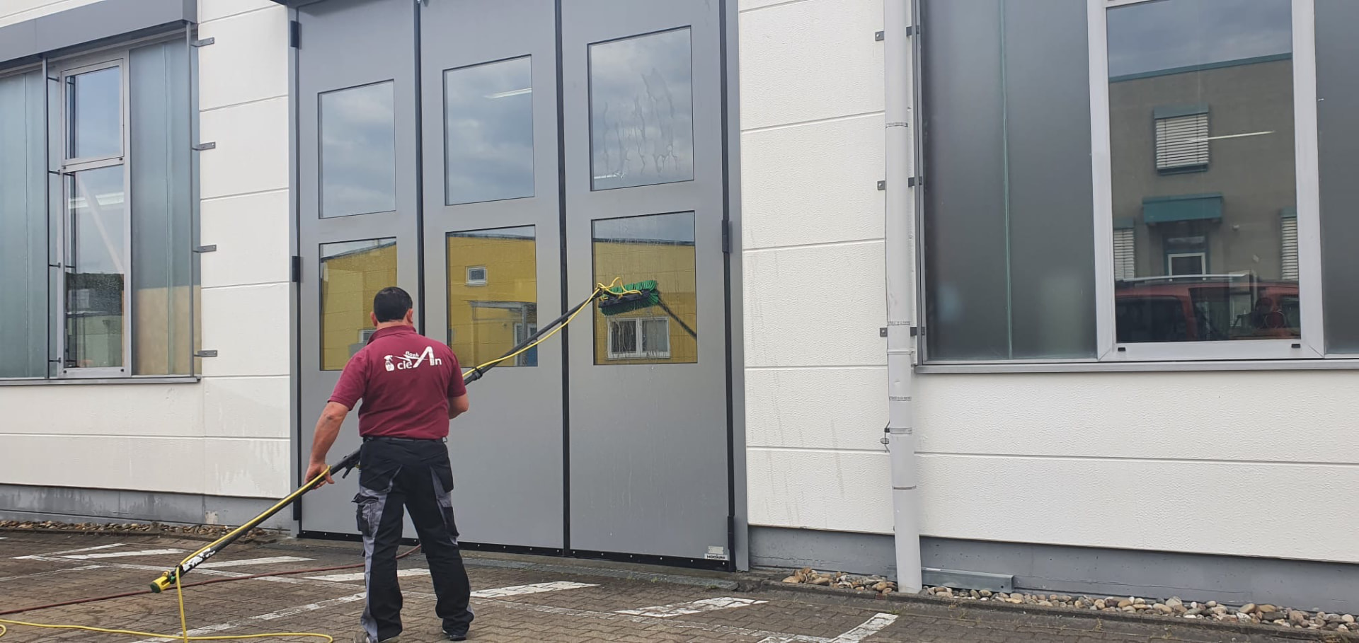 Mitarbeiter reinigt die Fensterfront einer Halle mit einer Teleskopstange